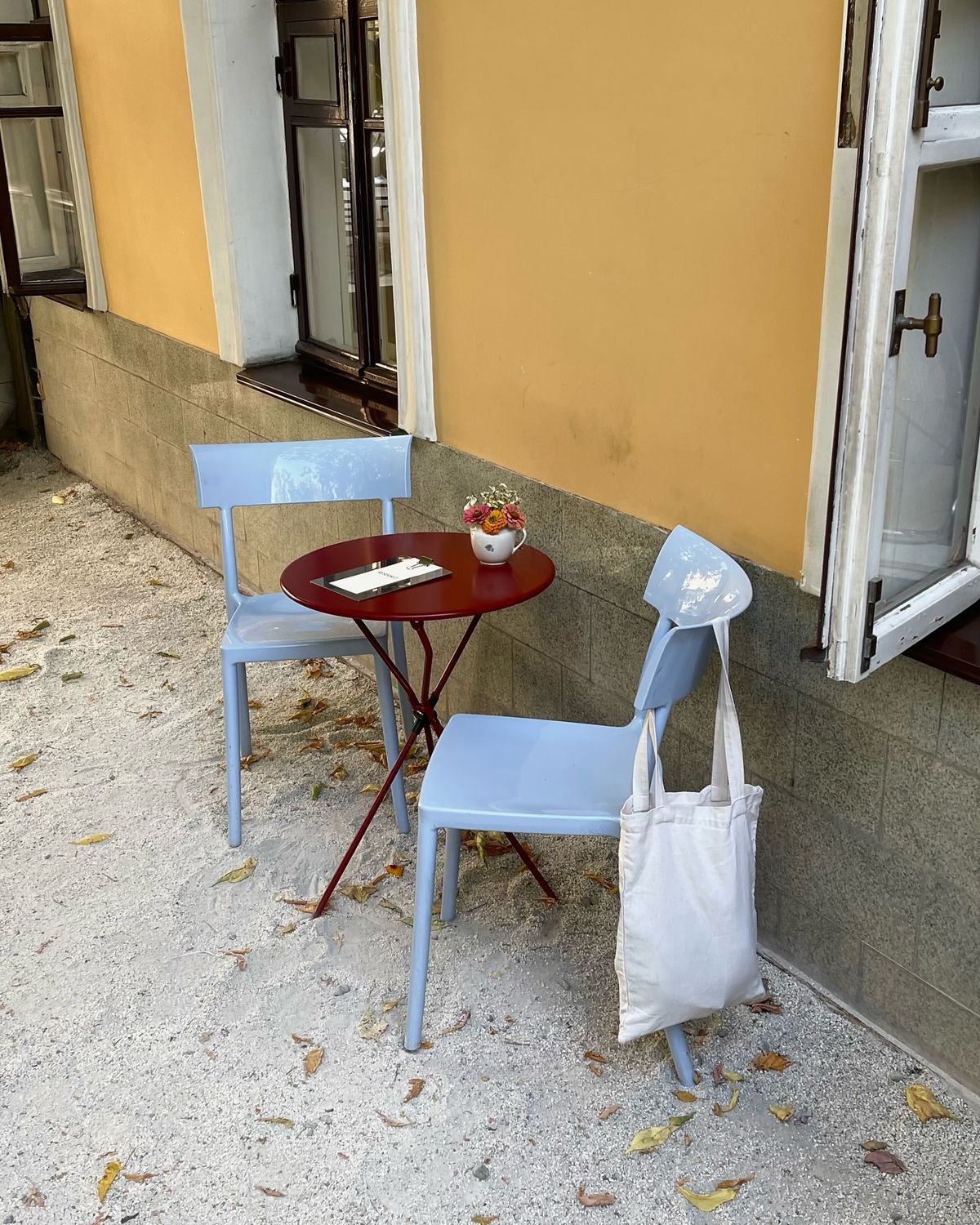 Zwei hellblaue Stühle an einem roten Bistrotisch vor dem Café
